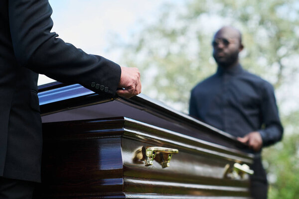 Two intercultural men in black attire closing coffin lid after farewell ceremony before carrying it to grave and burying dead person