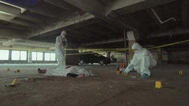 Terk edilmiş garajda cinayet davası üzerinde çalışan tanınmayan iki adli tıp dedektifinin yavaş çekimleri. Bir tanesi kamerada cesedin fotoğraflarını çekiyor ve meslektaşı da örnek ve kanıt topluyor.