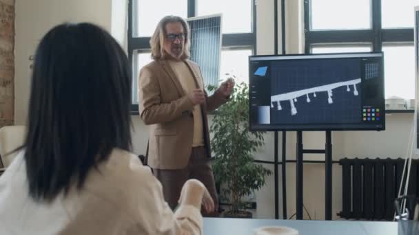 再生可能エネルギーシステム会社のオフィスに新しいソーラーパネルデザインを提示する白人男性エンジニアのミディアムフルショット および質問する聴衆からの女性リスナー — ストック動画