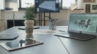 Yenilenebilir enerji açılışında mühendis masasının yakın plan görüntüsü, ekranda rüzgar türbini tasarımı resmi olan dizüstü bilgisayar, çalışma gününe başlamadan önce multimedya ekranında oynayan güneş panelleri hakkında video