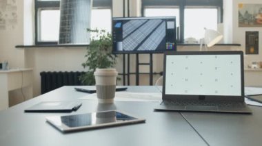 Yeşil enerji inşaat şirketindeki inşaat mühendisinin masasında beyaz ekranlı dizüstü bilgisayar, planlar, güneş panelleri, küçük ölçekli evler ve rüzgar türbini modelleri. Şablon, boşluğu kopyala