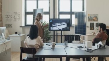 Kafkasyalı erkek mühendis, yenilenebilir enerji araştırma şirketinin ofisindeki dikkatli meslektaşlarına güneş paneli projesini multimedya ekranında sunuyor.