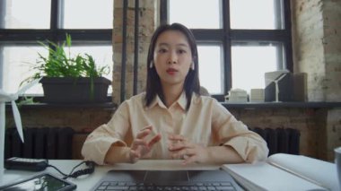 Genç, kendinden emin Çinli kadın mühendisin konferans sırasında dizüstü bilgisayarın önünde oturup iş arkadaşlarıyla konuşurken ve yeni taşınabilir güneş enerjili şarj aletini gösterirken orta boy görüntüsü.