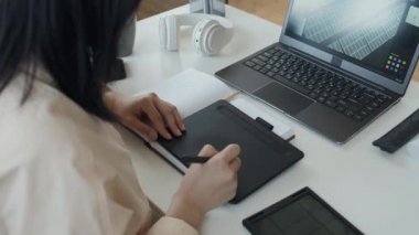 Masada oturan, Stylus 'la grafik tablet üzerinde çalışan ve dizüstü bilgisayardaki güneş paneli modelini manipüle eden tanınamayan Asyalı kadın mühendisin omuz üstü görüntüsü.