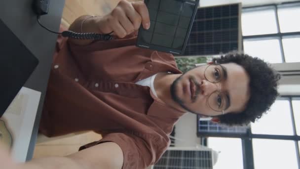 デスクに座っている若い多民族製品デザイナーの垂直撮影 企業ブログのビデオ更新 ソーシャルメディアでの新しいポータブルソーラー充電器の実演 — ストック動画