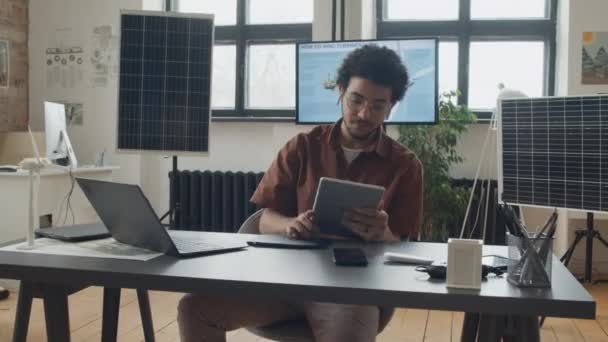 在可再生能源公司工作的中档男性工程师照片 在笔记本电脑上打字 在智能手机上讲话 使用图形平板电脑 背景是太阳能电池板原型 — 图库视频影像