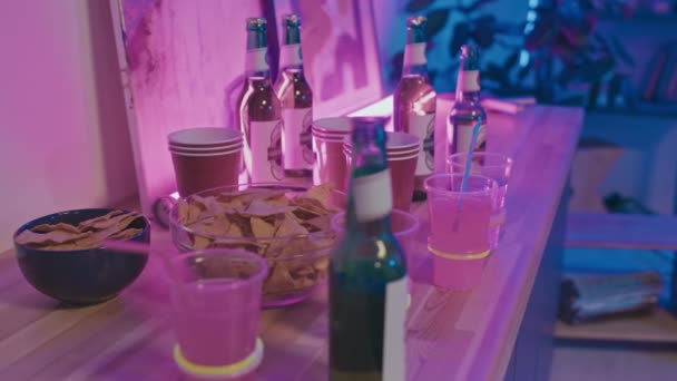 鸡尾酒 空纸杯和装有玉米片的碗的特写镜头放在桌上 在蓝色和粉色霓虹灯下 为家庭聚会做准备 — 图库视频影像