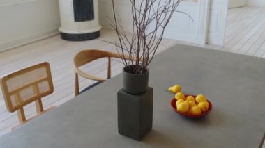 Siyah vazoda kurumuş ağaç dalının yakın plan görüntüsü, tabakta parlak sarı armutlar, bej dikdörtgen masa beyaz gölgeler içinde moda oturma odası, çağdaş minimalizm tarzında modern apartman dairesi