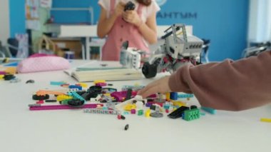 Robotik kulübünün masasında dikilmiş renkli plastik bloklar ve tuğlalardan oyuncak modeller yapan tanınmayan çocukların yakın plan fotoğrafları. Kiril RoboKuantum Yazısı