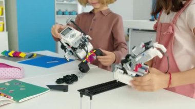 İki beyaz çocuğun okul sonrası hobi kulübünde robot modeller ve kablolar monte edip tasarım ve inşaatlarını tartışırken orta eğik çekimleri.