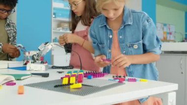 Okul çıkışında inşaat malzemeleriyle oynayan, elektrikli robot modeller yapan ve renkli plastik bloklarla bina inşa eden genç erkek ve kızların orta boy fotoğrafları.