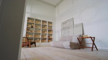 Geniş ev kütüphanesi, şık ahşap sandalye, kanepe ve masa ile dolu geniş ve havadar minimalist çağdaş dairede yüksek tavanlı, beyaz gölgeli