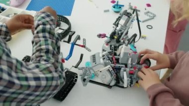 Okul sonrası hobi kulübünün masasındaki parlak plastik setlerden robot modeller tasarlayan çeşitli isimsiz çocukların yavaş çekimleri.