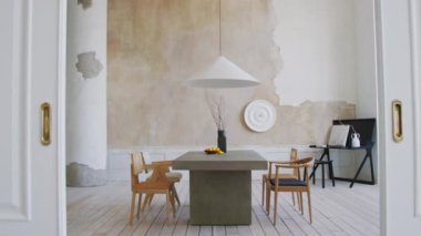 Yüksek tavan, sütun, dikdörtgen masa, ahşap sandalyeler ve yer döşemeleriyle döşenmiş lüks bir dairede, bej ve gri renkte minimalist iç dekorasyonlu devasa yemek odasının tam zoom görüntüsü.