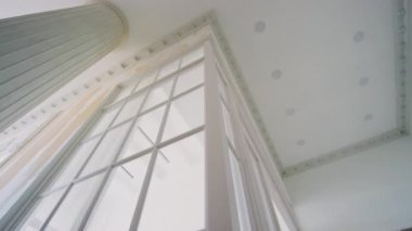 Lüks bir dairede düşük açılı tavan çekimi. Beyaz sütun, alçı pervazlar, spot ışıklar ve cam pencereler.