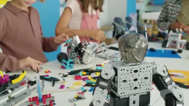 儿童俱乐部桌上的电动机器人的中档聚焦镜头 以及一群穿着休闲的多种族儿童用塑料建筑块建造自己的模型 — 图库视频影像