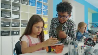 Orta boy beyaz gözlüklü kız ve inek Afrikalı Amerikalı çocuğun robot robot modelini birlikte çalışırken ve özelliklerini tartışırken, robotik hobi dersinde.