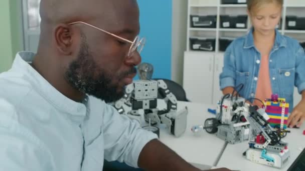 Zbliżenie Pochylenie Dół Ujęcie Afroamerykańskiego Nauczyciela Robotyki Męskiej Siedzi Przy — Wideo stockowe
