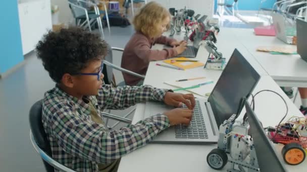 在课外机器人俱乐部与不同同学一起围坐在桌旁 用笔记本电脑编写机器人模型操作软件的中侧镜头 — 图库视频影像