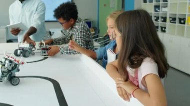 Orta boy bir grup genç Amerikalı öğretmen ve tabletle programlanabilir elektrikli robot modelleri izliyorlar. Okul sonrası robotik klübünde ders sırasında masada dönüyorlar.