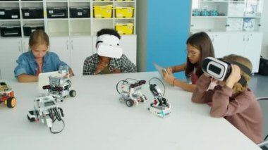Çok ırklı çocukların okuldan sonra IT kulübünde vakit geçirmesi. Tablet bilgisayar kullanan kızlar, VR kulaklık takan erkekler ve masada elektrikli robot modeller.