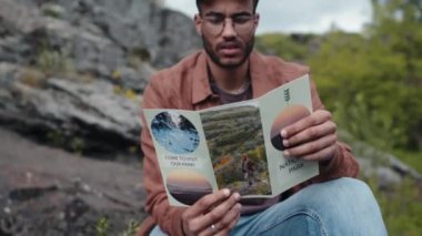 Genç erkek çift ırklı turistin broşür okurken, etrafa bakınırken ve şapkasını takarken.