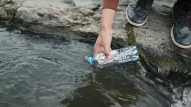 Nehirden su toplamak için kullanılan plastik şişeyi tutan tanınmayan birinin sığ odağı.