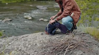 Sırt çantasından defter alıp çarşaflarını yakacak odunların altına koyan genç bir erkek çift ırklı turist.