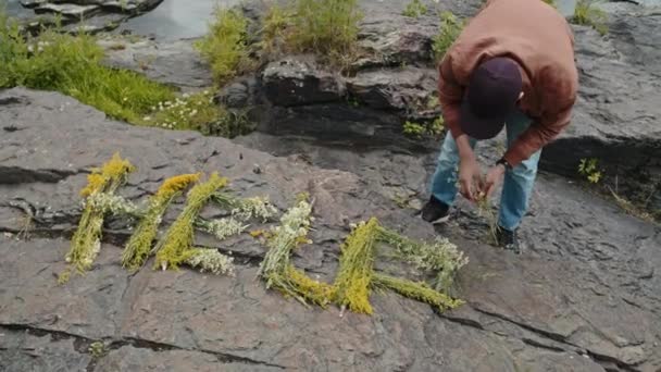 若い男性のBiracial観光客のチルトショットは 花からの助けのサインを作り 彼の帽子を振る — ストック動画