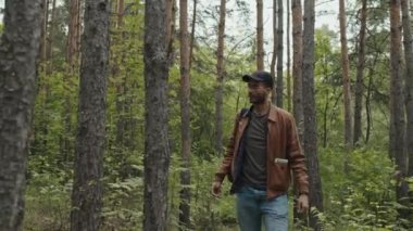 Geniş açılı genç erkek çiftçi turist ormanın içinde geziniyor ve geriye dönüp bakınıyor.