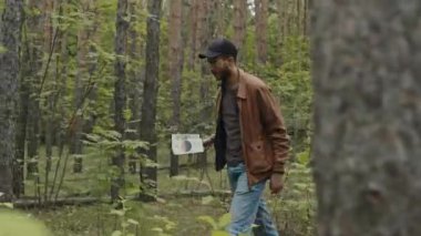 Genç erkek melez turistin broşür okurken, etrafa bakınırken ve ormanda yürürken çekilmiş yengeç fotoğrafı.