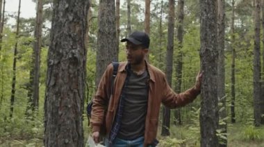 Orta boy erkek çift ırklı turist fotoğrafı. Yorgun ve kaybolmuş görünüyor. Ormanda yürüyor ve çıkış yolu arıyor.