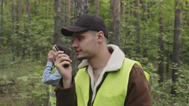 森の中を歩く緑の酸ベストで男性のコーカサス州のプロレスキューの追跡ショットとラジオセットで話す — ストック動画