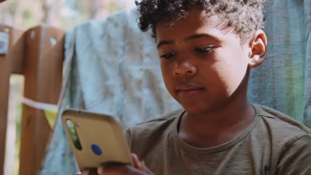 日光でスマートフォンでゲームをするアフリカ系アメリカ人の小学生のメディアクローズアップ — ストック動画