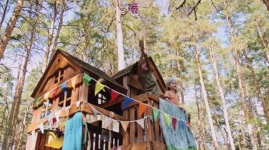 Afrika kökenli, ilkokul öğrencisi, ağaç evinden fırıldak oyuncağı sallayan, yanında duran, aynı yaştaki beyaz çocuk.