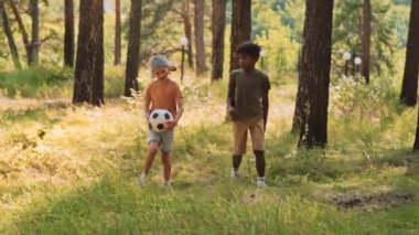 Afrika kökenli Amerikalı ve Kafkasyalı ilkokul çocukları ellerinde topla ormanda yürüyüp konuşuyorlar.