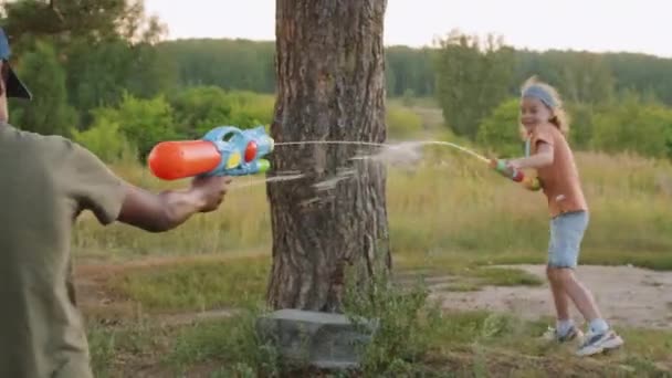 アフリカ系アメリカ人とコーカサス人の小学生のカメラシェイクは 日中の自然の中で水銃で遊んで幸せに — ストック動画