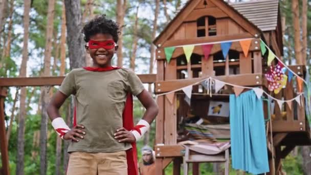 アフリカ系アメリカ人の小学生の肖像画は 遊び場のあるツリーハウスの前にスーパーヒーローの衣装を着ている — ストック動画