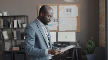 Erkek Afro-Amerikan ofis çalışanının gündüz ofisindeki belgelere gergin bir şekilde baktığı orta boy bir fotoğraf.
