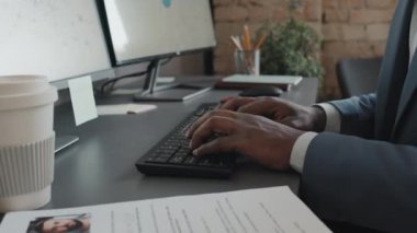 Gündüz vakti klavyeye bir şey yazan Afrikalı Amerikalı erkek ofis çalışanının ellerine odaklan.