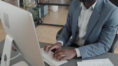 Afrika kökenli Amerikalı bir ofis çalışanının bilgisayarda çalışırken ve klavyeyle bir şeyler yazarken görüntüsü.