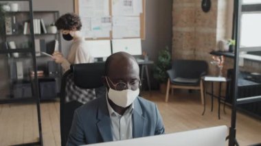 Afrika kökenli Amerikalı erkek ve Kafkasyalı ofis yöneticilerinin ofiste çalışan maske taktıkları bir fotoğraf.