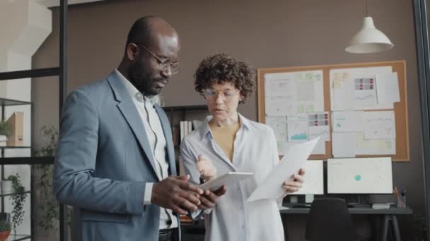 美国黑人和白人男性办公室职员在白天观看平板电脑和讨论办公项目的商业文件的中景照片 — 图库视频影像