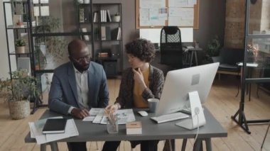 Afrika kökenli Amerikalı erkek ve beyaz kadın iş arkadaşlarının bilgisayar başında proje verileri ve görevlerini tartışırken geniş açılı görüntüleri
