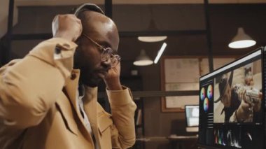 Afrika kökenli Amerikalı editörün kulaklık takıp akşamları ofisteki bilgisayar ekranına bakarken düşük açılı görüntüsü.
