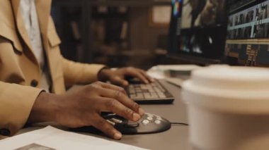 Ofiste masa başında oturan ve renk derecelendirme kontrolü kullanarak bilgisayarla çalışan erkek Afrikalı Amerikalı editörün ellerine odaklan