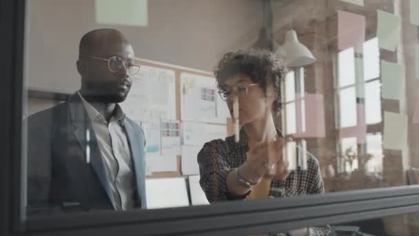 非洲裔美国人和白人男性办公室经理带着粘贴的字条盯着墙看的中景照片 — 图库视频影像