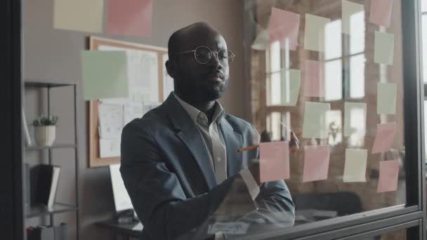 中镜头的非裔美国人办公室经理写在透明的墙上和点头的贴纸上 — 图库视频影像