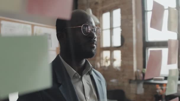 非洲裔美国男性办公室工作人员的中等特写镜头 他们看着透明的墙壁 上面粘贴着写着什么的便条 — 图库视频影像