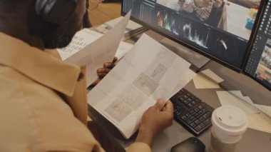 Erkek Afro-Amerikan editörün dokümanlara bakarken ve bilgisayar programındaki görüntülerle çalışırken çekilmiş görüntüleri.